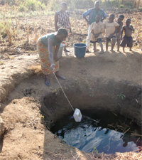 Woman collecting water with a rope and container.